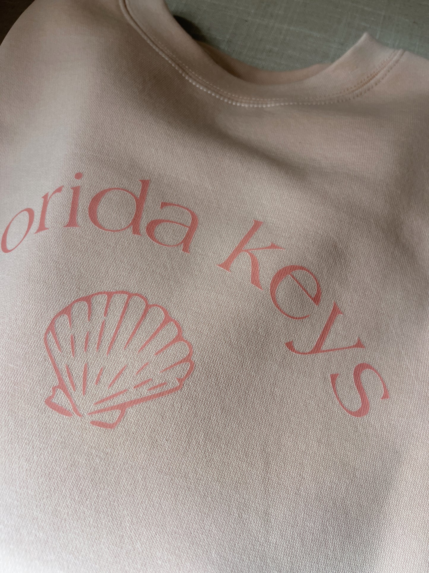 Folded pink sweatshirt with 'Florida Keys' and a shell design on a textured surface.