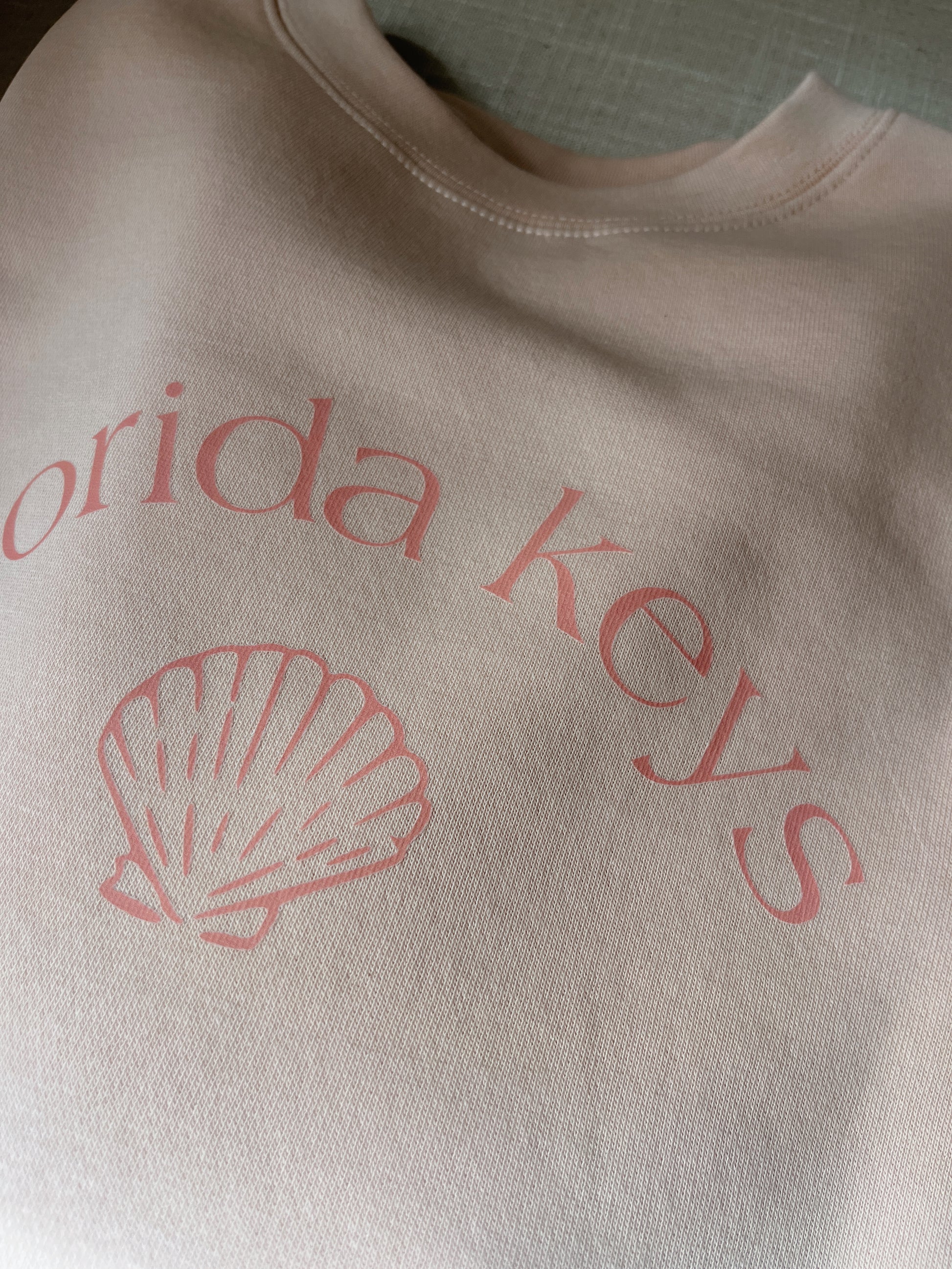 Folded pink sweatshirt with 'Florida Keys' and a shell design on a textured surface.