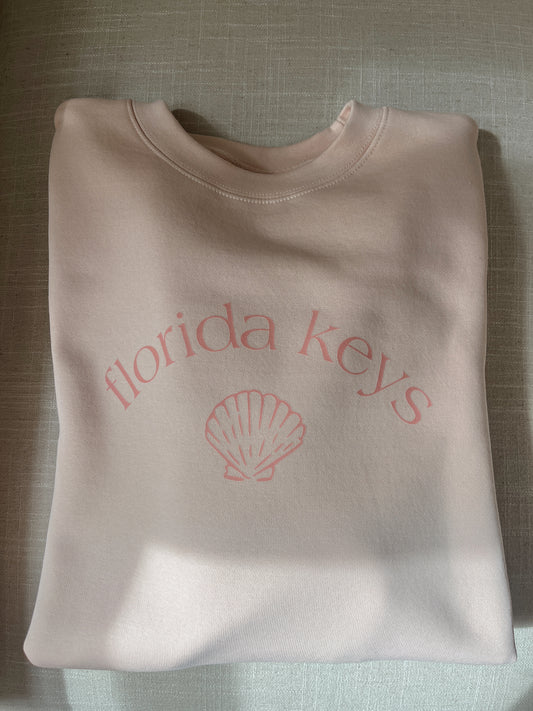 Folded pink sweatshirt with 'Florida Keys' and a shell design on a textured surface.